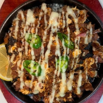 Sizzling beef sisig on a cast iron plate with green chilli, egg and calamansi