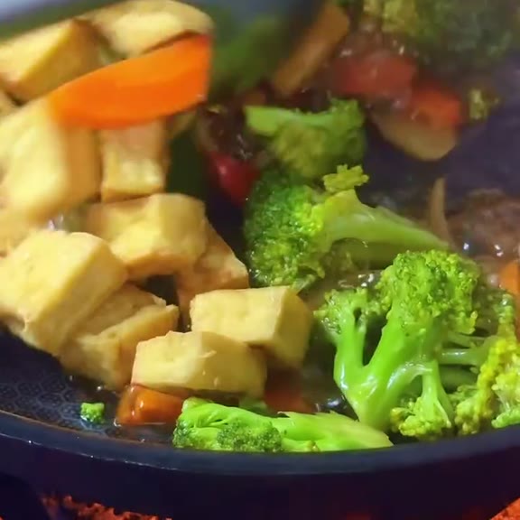 Golden fried tofu cubes, broccoli florets, carrot slices and red pepper simmering in brown sauce in a dark wok at Pinoy Tambayan