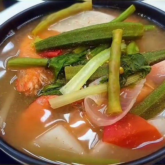 Bowl of sinigang na hipon with a whole orange shrimp, okra pods, water spinach stalks and leaves, sliced onion, red tomato and white radish in clear tamarind broth, served in a black bowl at Pinoy Tambayan