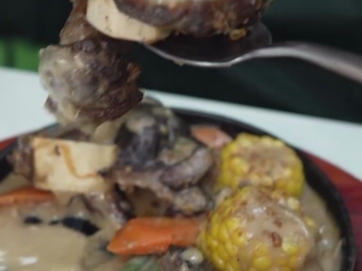 Beef shank and bone marrow with corn and carrots in gravy on a sizzling plate