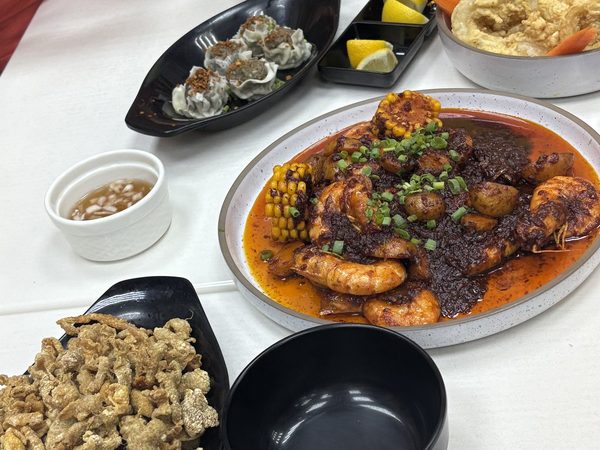 Shared table spread of Cajun prawns with corn and potatoes, steamed siomai, crispy chicken skin, battered calamari rings and lemon wedges.