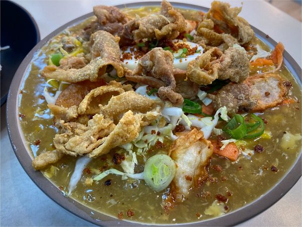 Bowl of lomi noodles in thick savoury gravy topped with crispy chicken skin, shredded cabbage, carrot, spring onion and a boiled egg.