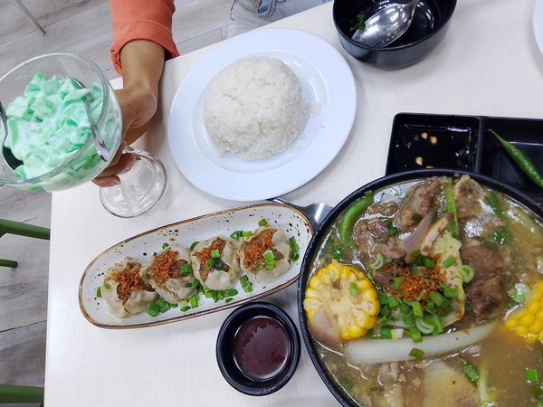 Overhead table spread with a bulalo beef shank hot pot, steamed siomai topped with fried garlic, plain rice and a glass of buko pandan.