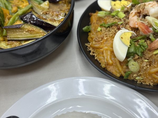 Pakbet of aubergine and string beans in squash sauce beside pancit Malabon topped with boiled egg, prawns, spring onion and a crisp crumb, with rice.
