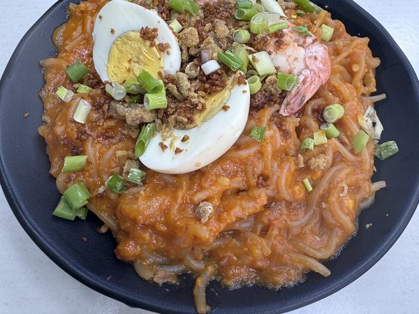 Pancit Malabon: thick rice noodles in orange sauce, topped with prawns, halved hard-boiled egg, crispy chicken skin, spring onions and a slice of lemon.