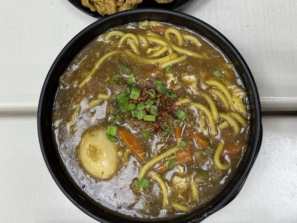Lomi noodle soup in thick broth with boiled egg, carrots, spring onion and fried garlic, served with crispy chicken skin, chilli oil, soy dip and lemon.